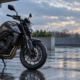 Motocicleta aparcada bajo una cubierta junto a un pavimento mojado y luz solar entre nubes