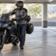 Motorista maniobrando a pie una moto grande en una plaza amplia de un aparcamiento cubierto