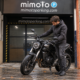 Motorista abrigado comprobando el apoyo lateral de su moto ante la entrada cerrada de MimoTo Parking Chamberí en otoño
