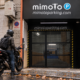 Motorista abrigado con su moto ante la entrada cerrada de MimoTo Parking Chamberí, con señalética de la marca y pavimento húmedo en otoño